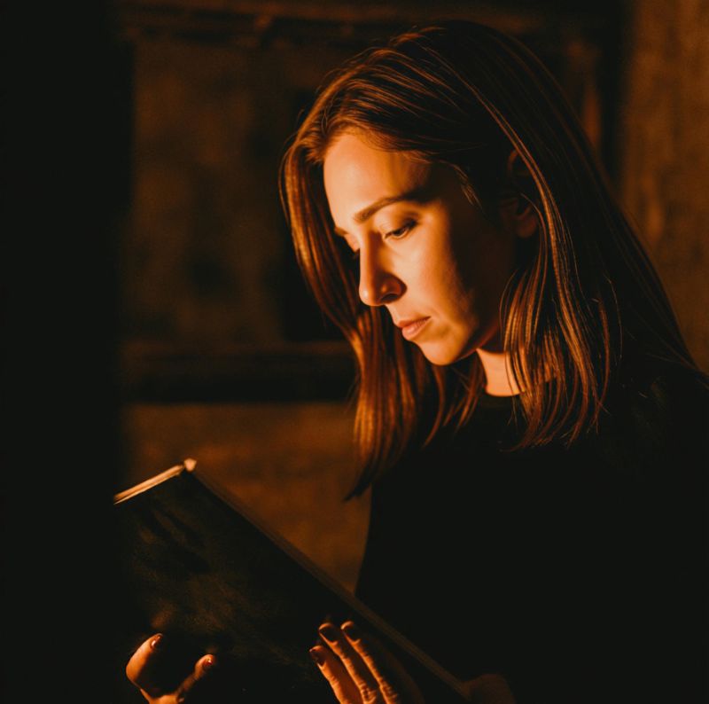 A woman davening from a siddur by candlelight